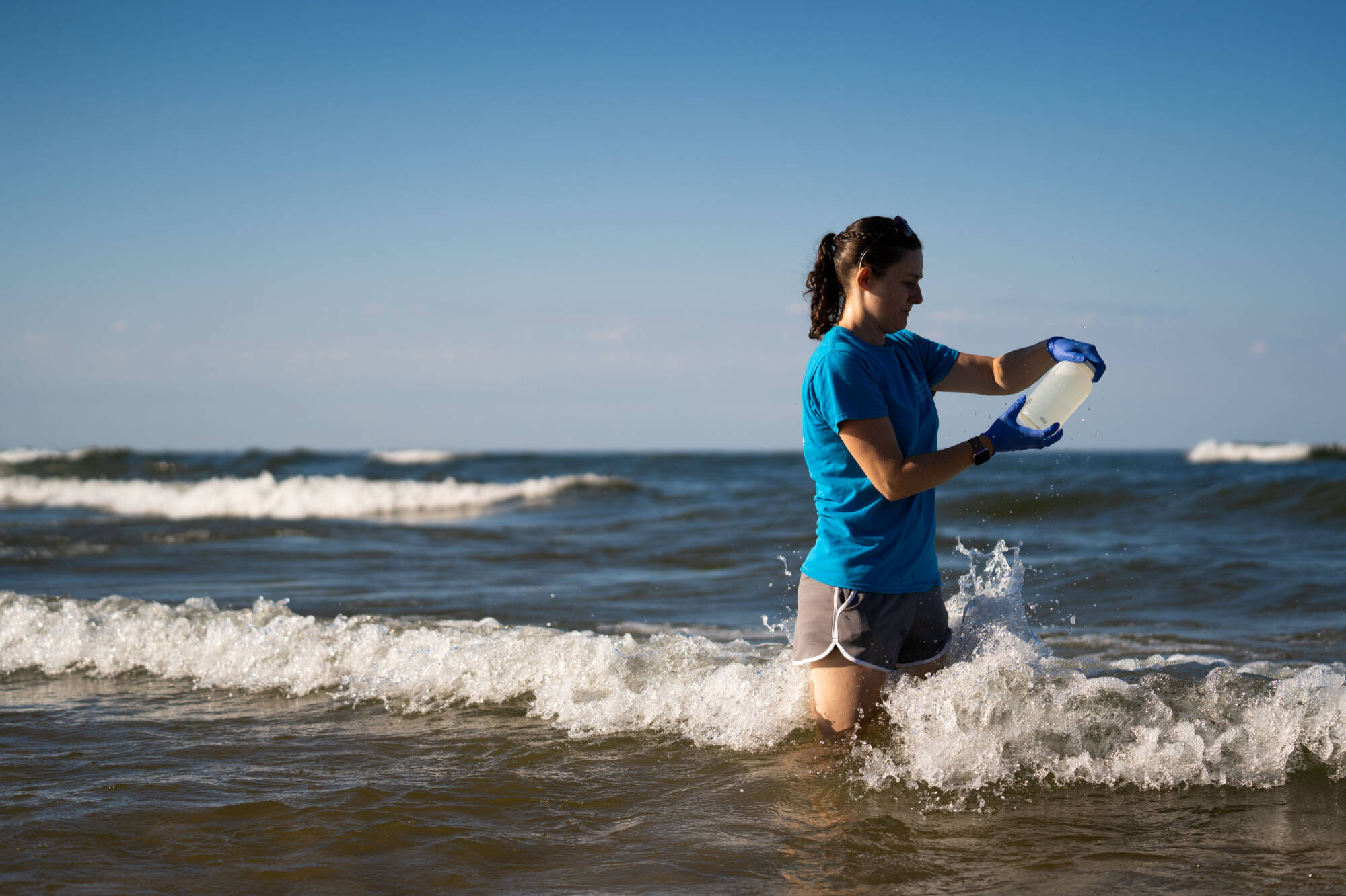 An AWRI researcher wades into the Lake Michigan surf to collect a bottle of water.